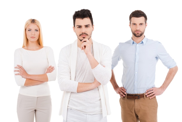 Confident young professionals. Three confident young people in smart casual wear looking at camera while standing against white background