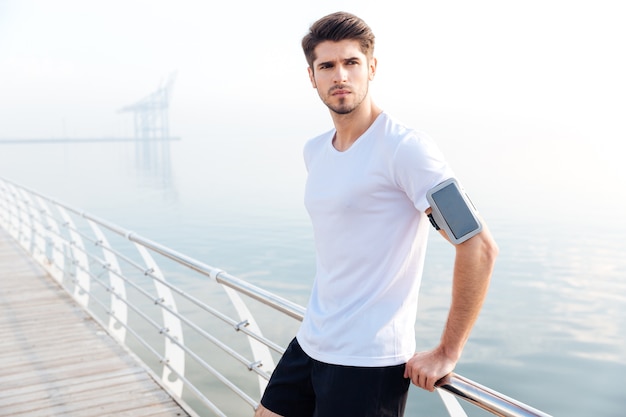 Confident young sportsman standing on pier and looking at the sea