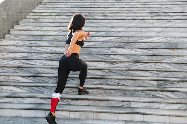 Confident young sportswoman running up the stairs outdoors