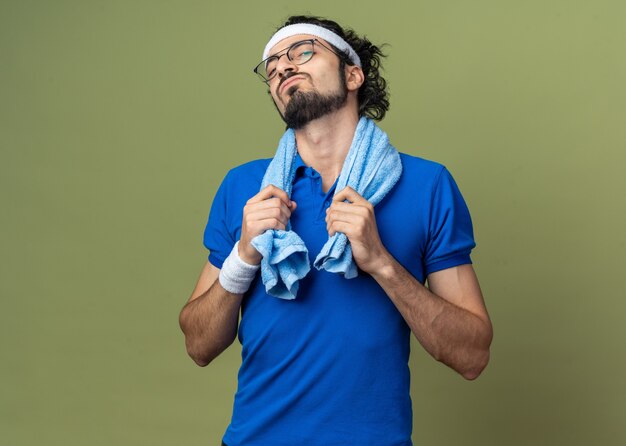 Confident young sporty man wearing headband with wristband and towel on shoulder 