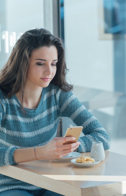 カフェでスマートフォンを使う自信のある若い女性