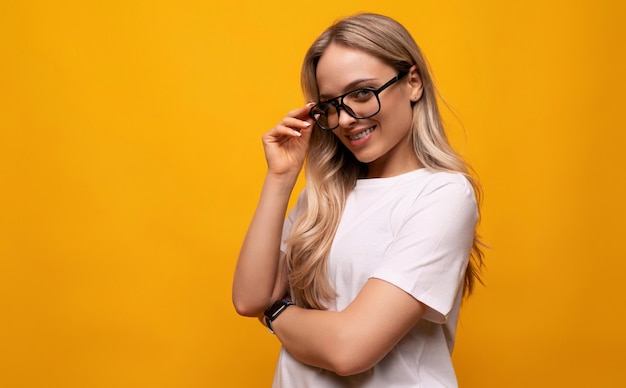 Confident young woman in glasses crossed her arms in front of her on a yellow background