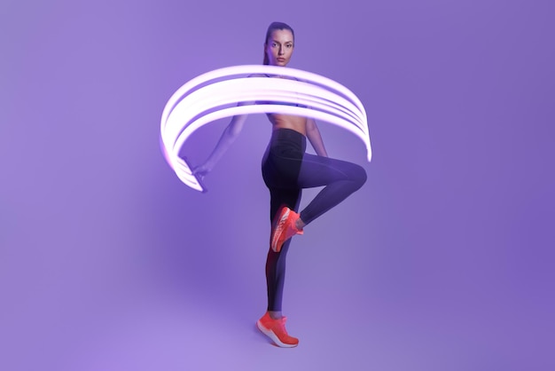 Confident young woman in sports clothing moving against violet background