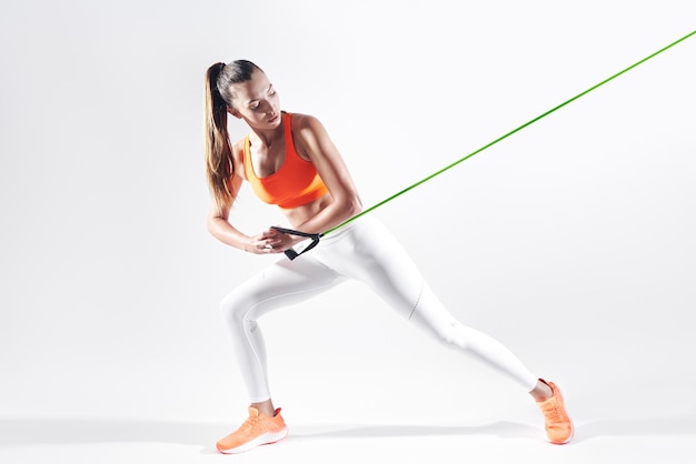 Confident young woman using resistance band while exercising against white background