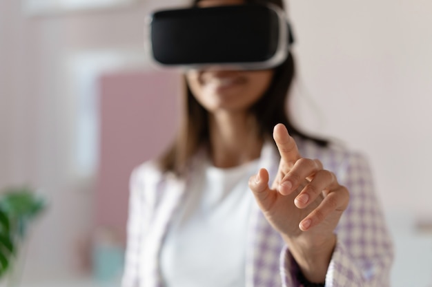 Foto fiduciosa giovane donna in cuffia per realtà virtuale che punta in aria mentre si trova al suo posto di lavoro in ufficio