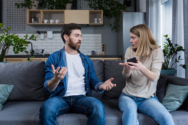 Conflict quarrel jealousy in the family home Young couple man and woman The woman is jealous takes the phone from her husband demands an explanation