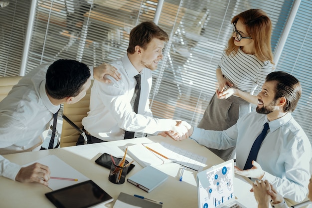 Conflict solved. Pleasant male office workers shaking hands, having reconciled with each other with the help of their colleagues and a team leader