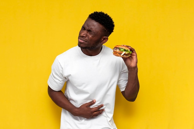 Photo confused african american man with stomach pain holding bad spoiled burger and suffering