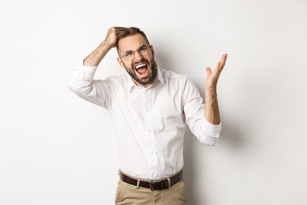 Confused and annoyed man scratching head, arguing and complaining, standing over white background.