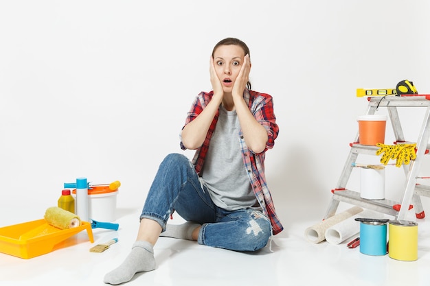 Confused annoyed tired shocked woman sitting on floor with instruments for renovation apartment isolated on white background. Wallpaper, accessories for gluing, painting tools. Concept of repair home.