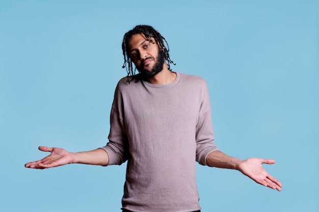 Confused arab man shrugging shoulders with pensive facial expression portrait. Young person standing and spreading hands wide while looking at camera with questioning emotions