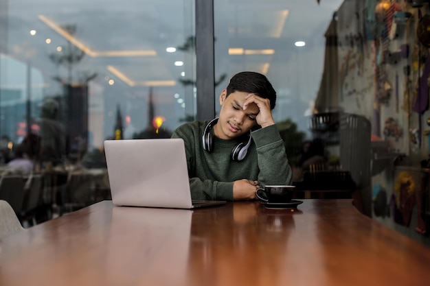 Confused Asian male college student while studying using a laptop at the cafe or coffee shop