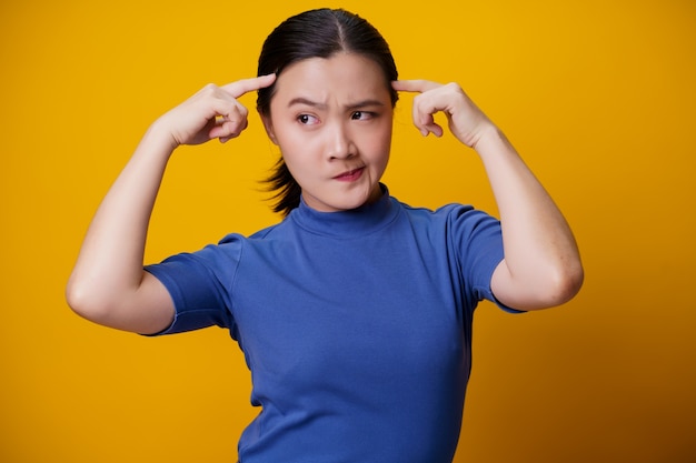 Confused Asian woman thinking and standing on yellow.