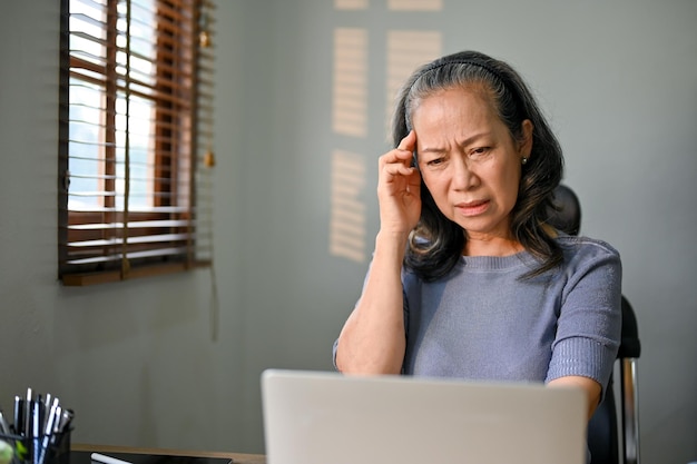 Confused Asianaged woman having a problem with her internet connection on her laptop