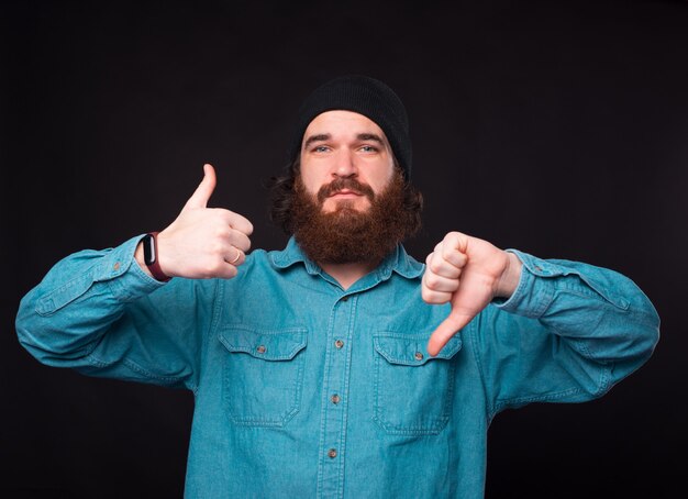 Фото Смущенный бородатый мужчина демонстрирует жесты одновременно и нравится, и не нравится.