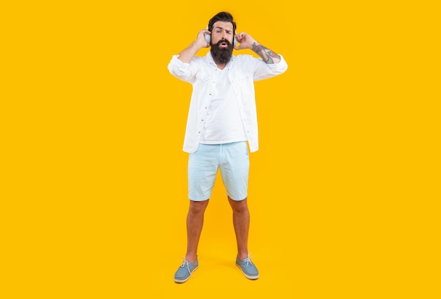 Confused bearded man listening music in headphones isolated on yellow man listening music