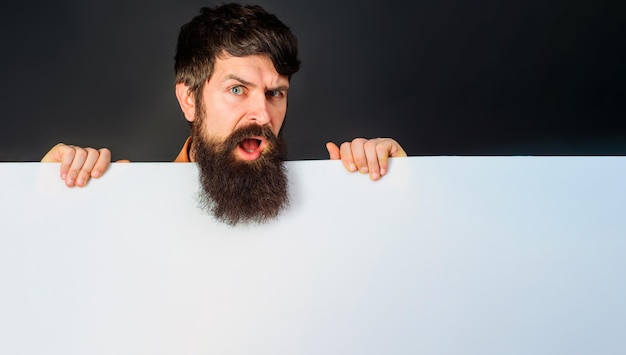 Confused bearded man with advertising banner handsome guy shows empty board with space for text