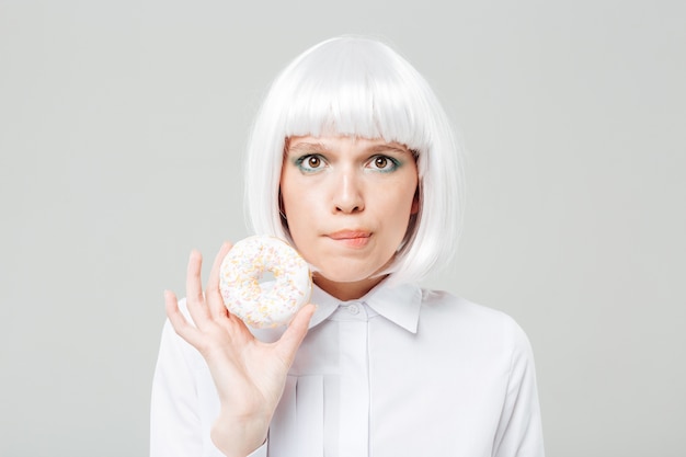 Confused beautiful young woman holding sweet donut