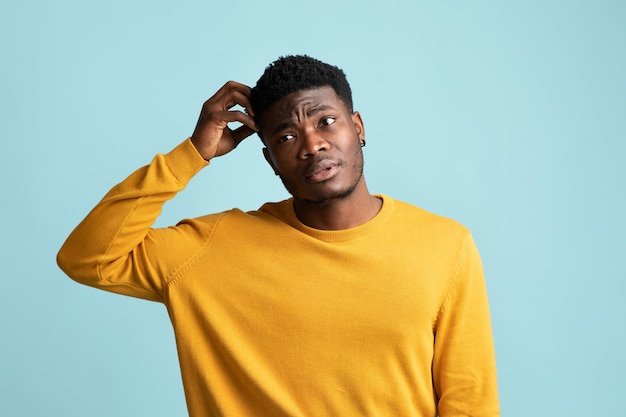 Confused black guy touching his head blue background