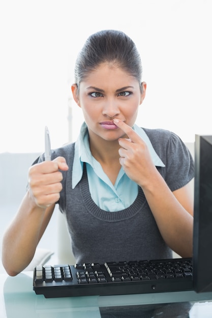 Confused businesswoman with pen at office desk