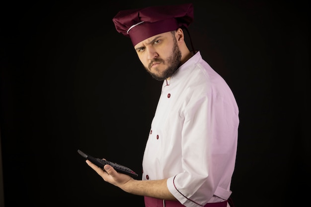 Confused chef man holds calculator suspiciously