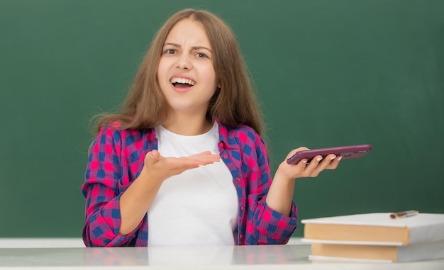 confused child at school chatting on phone on blackboard background, sms.