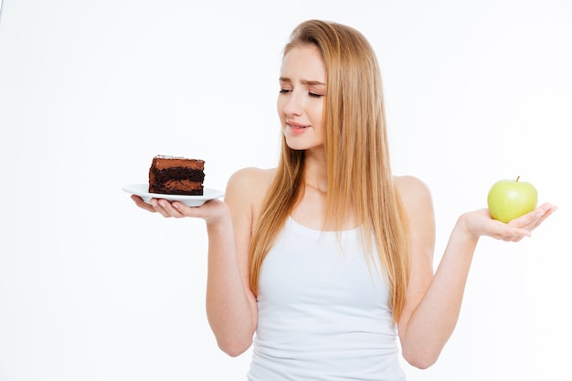 Confused cute young woman choosing between healthy and unhealthy food over white background