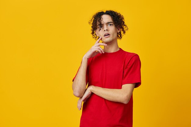 Confused funny caucasian young man in red tshirt can not make\
decision posing isolated on over yellow studio background the best\
offer with free place for advertising emotions for everyday\
concept