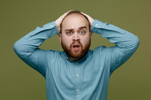 Confused grabbed head young handsome guy wearing blue shirt isolated on green background