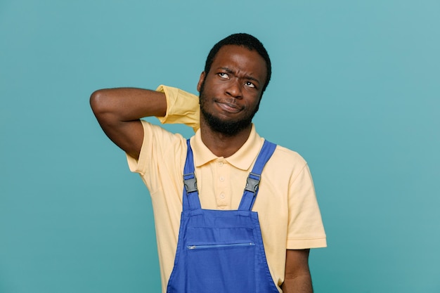 Смущенный схватил за шею молодого афроамериканца-уборщика в униформе с перчатками, изолированными на синем фоне