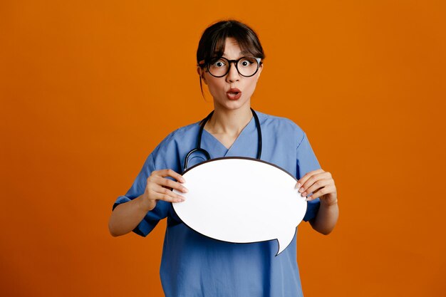 Photo confused holding speech bubble young female doctor wearing uniform fith stethoscope isolated on orange background