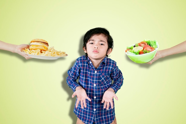 Confused little boy choosing a salad or hamburger