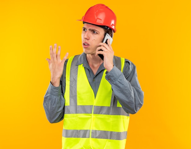 Confused looking at side young builder man in uniform speaks on phone 