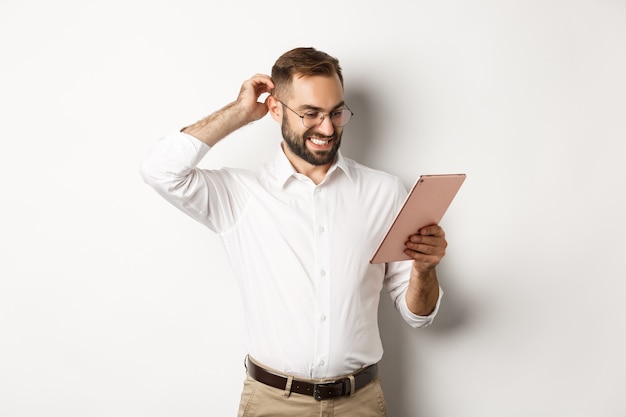 Confused male manager looking puzzled at digital tablet, scratching head doubtful, standing over white background.