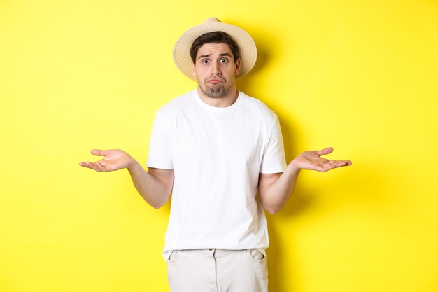 Confused male tourist shrugging, looking indecisive, standing against yellow wall