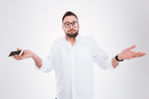 Confused man holding phone isolated over white wall.