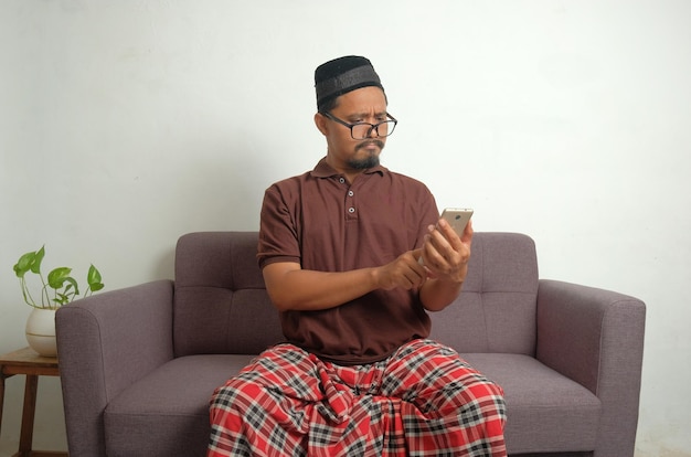 Confused man looking phone screen while sitting in sofa