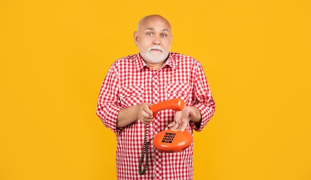 Confused old man with vintage telephone on yellow background