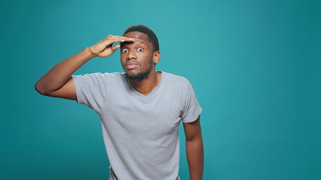 Confused person using hand over forehead to look around, searching for clue in distance. Young adult looking forward, having interest in exploration and feeling pensive, confident man with curiosity.