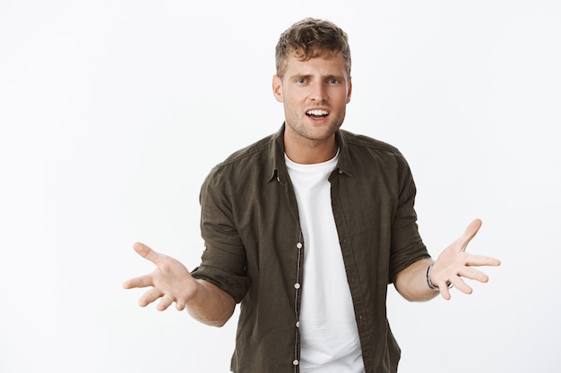 Confused and pissed guy just cannot understand what womanfriend wants, arguing demanding explanations holding hands sideways is daze and dismay frowning clueless and annoyed over gray wall