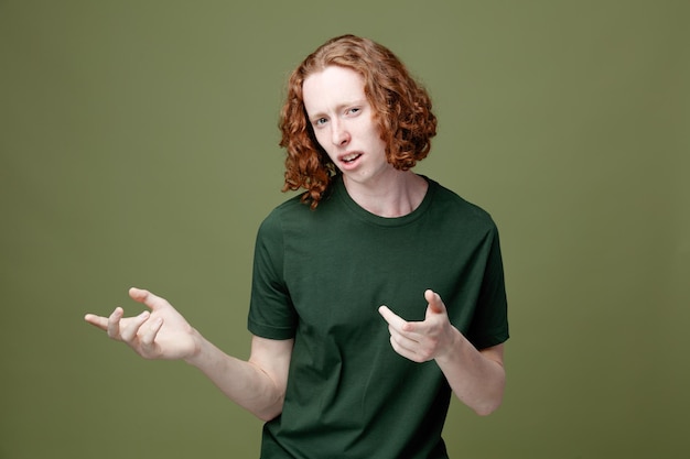 Confused points at side young handsome guy wearing green t shirt isolated on green background