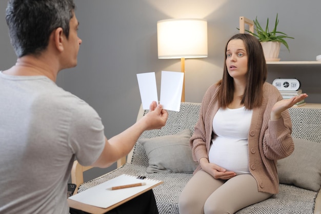 Photo confused puzzled regnant woman visiting psychologist doctor male psychotherapist showing picture to woman client at session in an office female with uncertain face during consultation