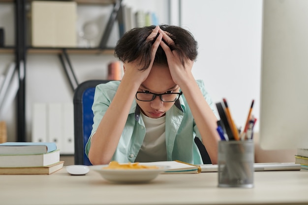 Scolaro confuso che guarda il suo libro di testo con un'equazione difficile che deve risolvere