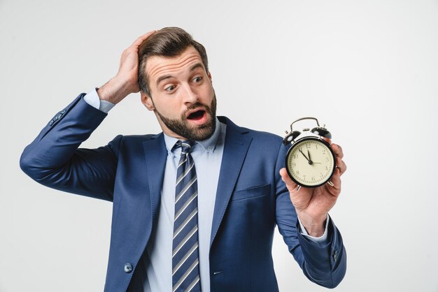 Photo confused shocked caucasian young businessman ceo manager freelancer teacher holding alarm clock for deadline being late high time for sale discount offer isolated in white background