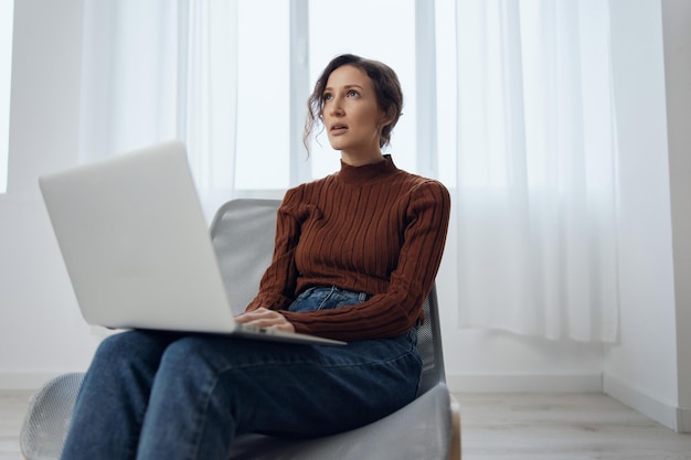 Confused thoughtful upset young frustrated adorable curly woman
with laptop think about difficult life decision looks up can not
choose sitting in chair at home social media online
communication