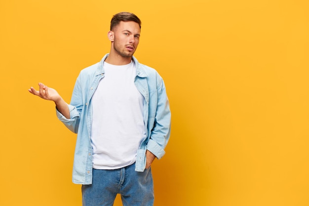 Confused unhappy tanned handsome man in blue basic tshirt raise\
hand up look at camera posing isolated on orange yellow studio\
background copy space banner mockup people emotions lifestyle\
concept