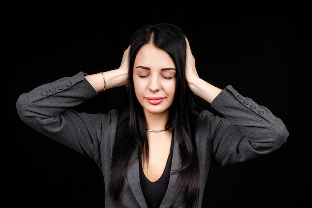 Confused woman holding hands on head over black studio background. Portrait of young serious girl closing her ears, hear no evil, deafness concept, copy space.