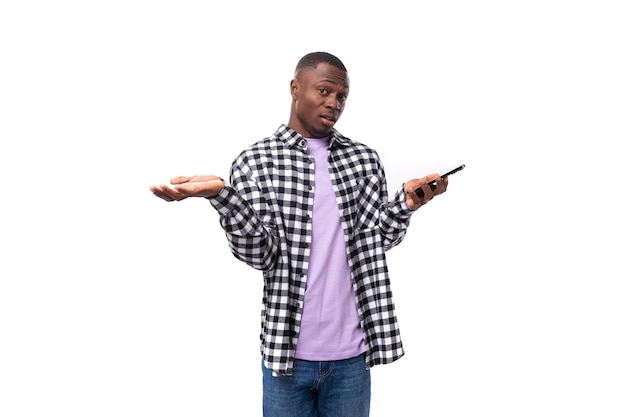 Confused young american man in plaid shirt looking at phone on white background with copy space