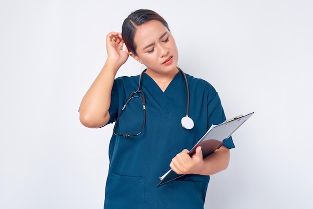 Confused young asian woman nurse wearing a blue uniform with a
stethoscope looking at a clipboard isolated on white background
healthcare medicine concept