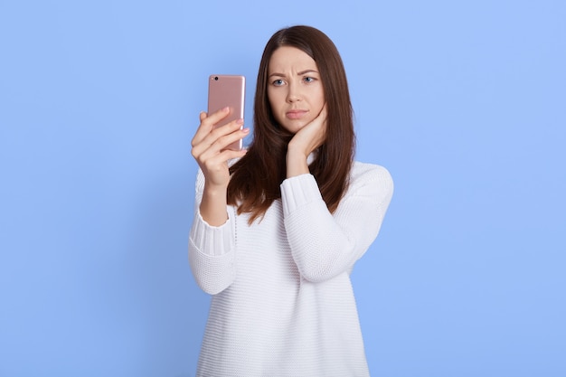 Giovane bella donna confusa che posa isolata sopra l'azzurro